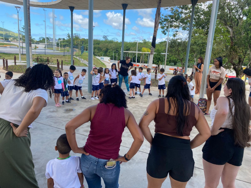 Crianças e pais realizam alongamento com a professora de Educação Física Vanisse, participando juntos de um momento de movimento, integração e bem-estar.